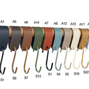 May include: A collection of S-shaped hooks in various colors, including black, brown, green, and white, hanging from a wooden rod. Each hook has a matching strap. The hooks are labeled with alphanumeric codes.