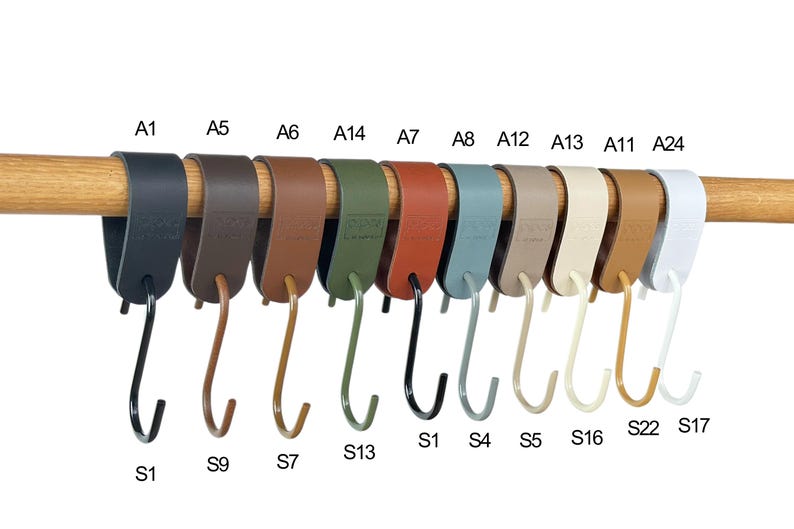 May include: A collection of S-shaped hooks in various colors, including black, brown, green, and white, hanging from a wooden rod. Each hook has a matching strap. The hooks are labeled with alphanumeric codes.