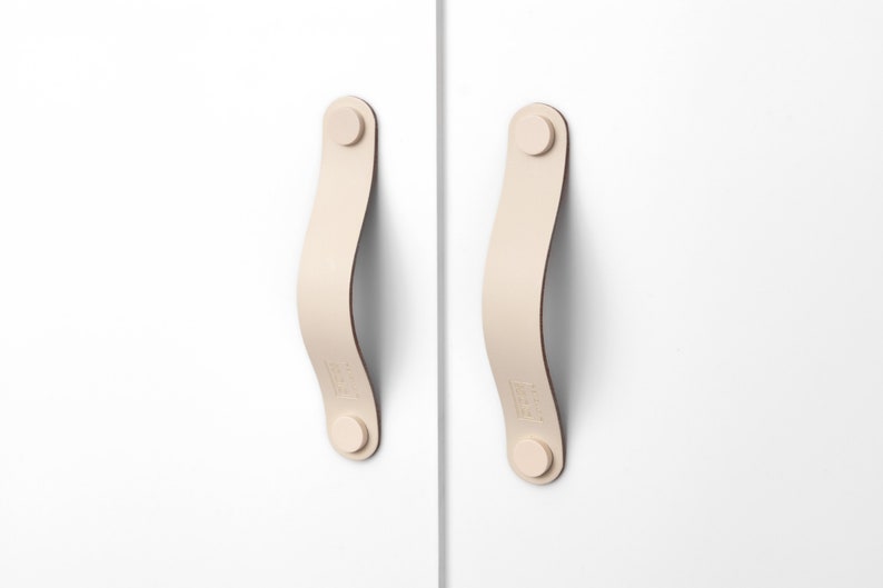 May include: Two off-white leather cabinet pulls with rounded edges and a small round knob at each end.