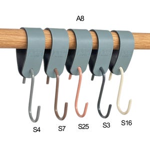 May include: A row of six gray, over-the-rod hooks with different colored hooks: gray, brown, pink, black, and cream. The hooks are hanging on a wooden rod. The text "A8" is above the hooks, and the text "S4", "S7", "S25", "S3", and "S16" are below.