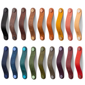 May include: Twenty leather cabinet pulls in a variety of colours, including black, brown, blue, green, purple, red, and orange. Each pull has a curved shape and two round metal ends.