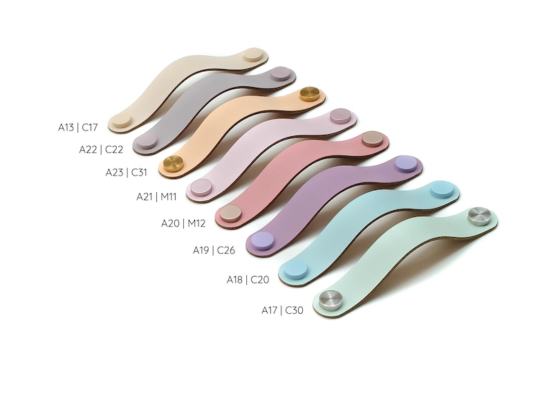 May include: A collection of eight curved leather drawer pulls in various pastel and neutral colors, including beige, gray, tan, pink, lavender, blue, and mint. Each pull features two circular metal or matching leather fasteners at the ends.