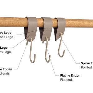 May include: Three taupe-colored, S-shaped hooks suspended from a wooden rod. The hooks are designed to hang items. The image includes text labels in German and English, indicating different hook features.