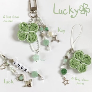 May include: A collection of handmade keychains and charms featuring green crocheted four-leaf clovers, beads, and star-shaped accents. The word "Lucky" is written in green script. Includes a silver-tone key ring and a white lanyard.