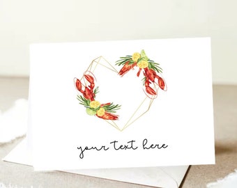 May include: White greeting card with a watercolor design of a gold geometric heart shape, adorned with red lobsters, lemon slices, and greenery. The text "your text here" is written in black script.