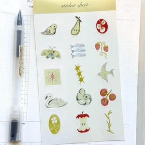 Pode incluir: Uma folha de autocolantes com vários desenhos ilustrados, incluindo um pássaro, uma pera, peixes, uma borboleta, morangos e um cisne. A folha tem o texto "sticker sheet" no topo. Uma caneta transparente com tinta preta está à esquerda.