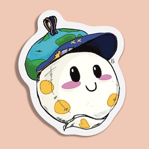 Puede incluir: Una pegatina caprichosa con un personaje redondo y sonriente con mejillas rosadas y ojos negros. Lleva un sombrero de mago azul y dorado con estrellas y un sombrero con forma de globo. El personaje tiene manchas amarillas y un diseño cosido.