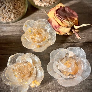 May include: Three clear resin rose-shaped bottle stoppers with gold glitter accents. The stoppers are on a wooden surface.