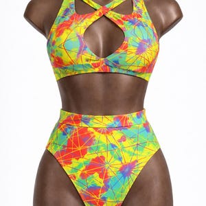 May include: A two-piece swimsuit with a vibrant, abstract pattern in yellow, red, blue, and green. The top features a criss-cross halter design with a keyhole cutout. The high-waisted bottoms complete the set, displayed on a mannequin.