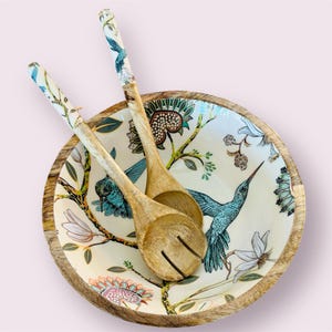 May include: A wooden salad bowl with a white background and a colorful floral pattern featuring hummingbirds. The bowl comes with two wooden serving spoons.