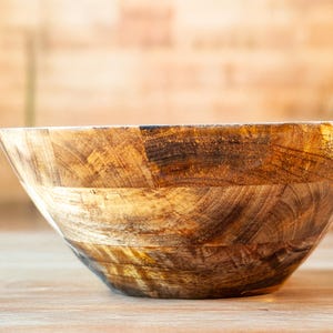 May include: A large, wooden bowl with a natural, rustic finish. The bowl is made of multiple pieces of wood that have been joined together to create a unique pattern.