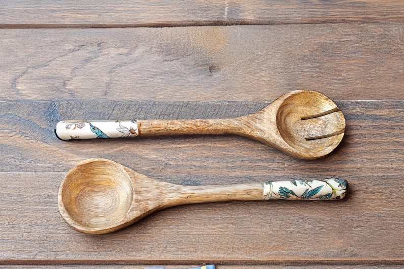 May include: Two wooden spoons with floral patterned handles. The spoon on the left is a serving spoon, while the spoon on the right is a slotted spoon.