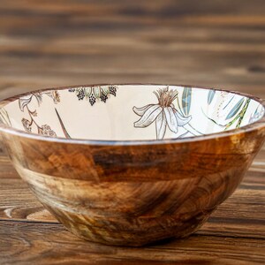 May include: A wooden bowl with a white interior and a floral design. The bowl is made of natural wood and has a rustic look.
