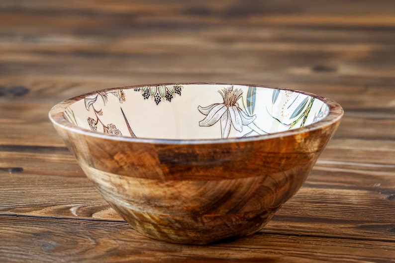 May include: A wooden bowl with a white interior and a floral design. The bowl is made of natural wood and has a rustic look.