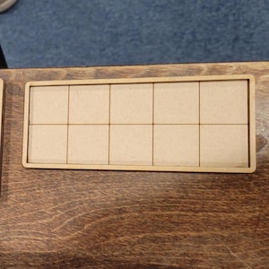 May include: A rectangular wooden tray with ten equally sized square compartments. The tray is made of light brown wood and has a darker brown border. The tray is sitting on a dark brown wooden surface.