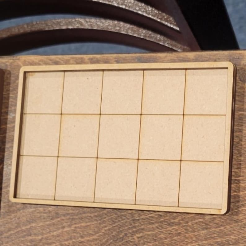 May include: A rectangular wooden tray with a grid of 15 squares. The tray is light brown and appears to be made of plywood or a similar material. The grid lines are thin and precisely cut, creating a neat, organized appearance.