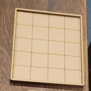 May include: A square, light-colored wooden tray with a grid pattern. The tray is divided into 25 equal squares, each approximately 1.5 inches by 1.5 inches. The edges of the tray are slightly raised, creating a border.