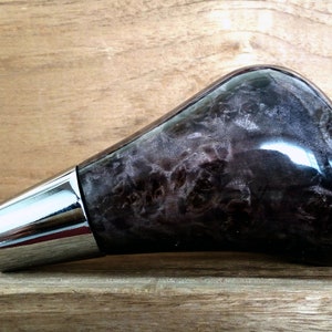 May include: A black and silver gear shift knob with a wood grain pattern. The knob is made of a durable material and has a sleek, modern design.