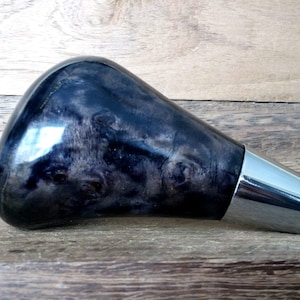 May include: A black and grey wood gear knob with a chrome accent. The knob is shaped like a teardrop and has a smooth, polished finish.
