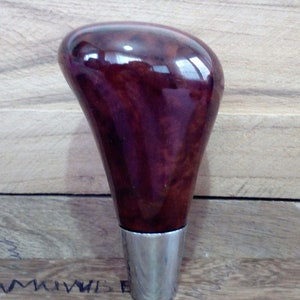 May include: A dark brown wooden gear shift knob with a silver metal base.
