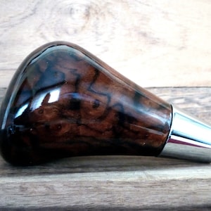 May include: A dark brown wood gear shift knob with a chrome tip. The wood has a unique grain pattern.