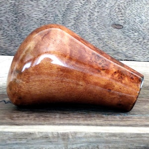 May include: A brown wooden gear shift knob with a unique wood grain pattern. The knob has a smooth, polished finish.