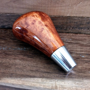 May include: A wooden gear shift knob with a brown wood grain and a silver metal base.
