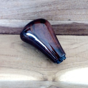 May include: A dark brown wooden gear shift knob with a black plastic base.