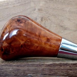 以下が含まれることがあります： 銀色の金属製のベースが付いた茶色の木製のシフトノブ。ノブには独特の木目模様があります。