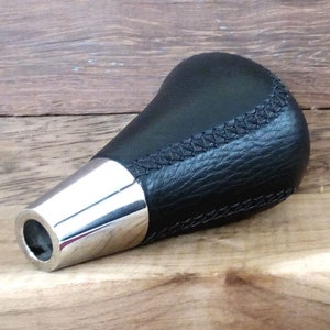 Könnte beinhalten: Schwarzer Leder-Schalthebelknauf mit verchromter Basis. Der Knauf hat ein genähtes Design.