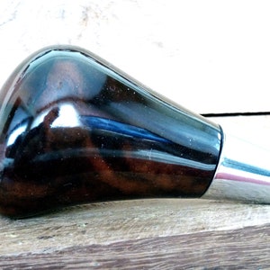 May include: A dark brown wooden gear shift knob with a silver metal trim. The knob has a smooth, polished finish.