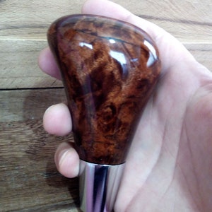 May include: A brown wooden gear shift knob with a silver metal base. The knob has a unique wood grain pattern.