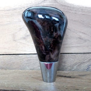 May include: A dark brown wooden gear shift knob with a silver metal base. The knob has a unique wood grain pattern.