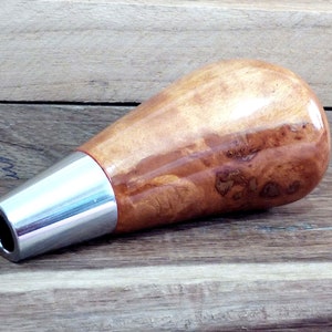 May include: A wooden and chrome bottle stopper with a unique burl wood design. The stopper is shaped like a teardrop and has a chrome metal base.