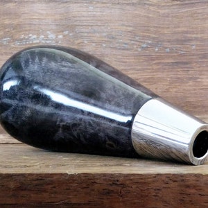 May include: A black and white wood gear stick knob with a silver metal collar. The knob is shaped like a teardrop and has a smooth, polished finish.