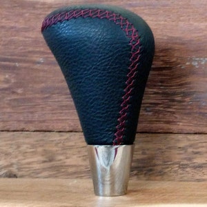May include: Black leather gear shift knob with red stitching and a silver base.