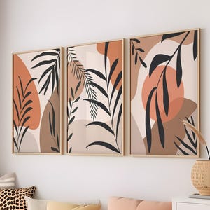 May include: Three abstract art prints with a minimalist design featuring brown, beige, and orange colors. The prints depict stylized leaves and organic shapes.