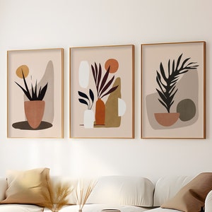 May include: Three framed abstract art prints with a minimalist style. Each print features a potted plant with a brown, beige, and green color scheme.