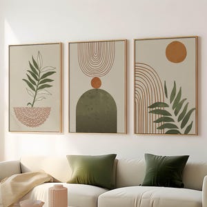 May include: A set of three framed wall art prints featuring abstract designs in muted tones. The prints display green botanical leaves, terracotta-coloured arches, and circular shapes on a light beige background, all encased in thin wooden frames.
