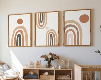 May include: Three framed art prints with abstract rainbow designs in neutral tones of brown, beige, and green. The artwork is displayed above a wooden cabinet with decorative items, including candles and a vase of flowers. A crib and chair are also in the room.