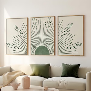 May include: Three framed prints featuring a green sunburst design on a cream background. The sunburst design is made up of thin lines and small circles. The frames are a light wood colour.