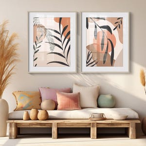May include: Two framed abstract art prints with a neutral color palette of beige, brown, and peach. The prints feature stylized leaves and organic shapes.