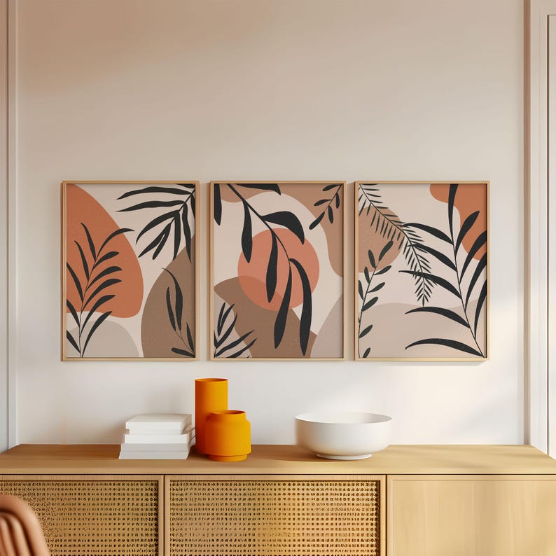May include: Three framed prints with abstract botanical illustrations in shades of brown, orange, and cream. The prints feature stylized leaves and organic shapes.