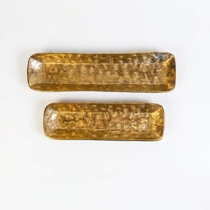 May include: Two rectangular serving trays with a hammered gold finish. The trays are different sizes and are placed on a white background. The trays have rounded corners and a textured surface.