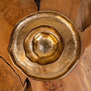 May include: A set of three gold-colored decorative bowls. The bowls are nested, with a large, shallow bowl on the outside, a medium-sized bowl in the middle, and a small, hexagonal bowl in the center. The bowls have a textured surface and a metallic sheen.