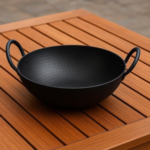 May include: Black metal serving bowl with hammered texture and two handles. The bowl is sitting on a wooden table.