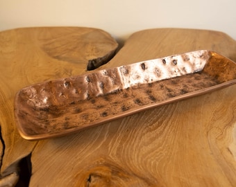 May include: A rectangular copper tray with a hammered texture. The tray has rounded corners and is displayed on a wooden surface. The copper has a warm, reddish-brown color.