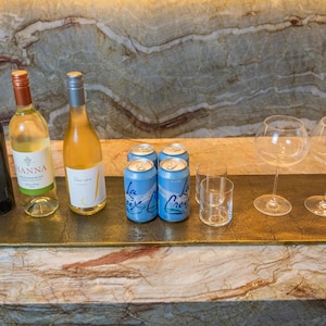 Może przedstawiać: Prostokątna, złota taca do serwowania z butelkami wina, puszkami La Croix, szklankami i kieliszkami do wina. Butelki zawierają czerwone i białe wino. Puszki La Croix są jasnoniebieskie. Szklanki są przezroczyste.