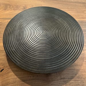 May include: A black wooden round serving tray with concentric circles carved into the surface.