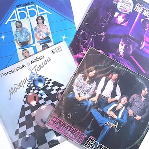 Könnte beinhalten: Vier quadratische Vinyl-Schallplattencover mit ABBA Voulez-Vous in Blau, The Moody Blues in Lila, Modern Talking mit Schachbrettmuster und Smokie mit einem Bandporträt. Jedes Cover zeigt Bandnamen und Titel in verschiedenen Schriftarten.